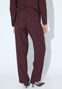 Pantalons larges bordeaux en tissu lisse, dotés d'une poche arrière et d'une taille haute, associés à des escarpins noirs à talons pointus.