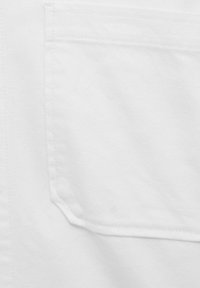 Tejido blanco texturizado con un gran bolsillo de parche que presenta detalles de costura visibles. Diseño liso y limpio sin adornos adicionales.