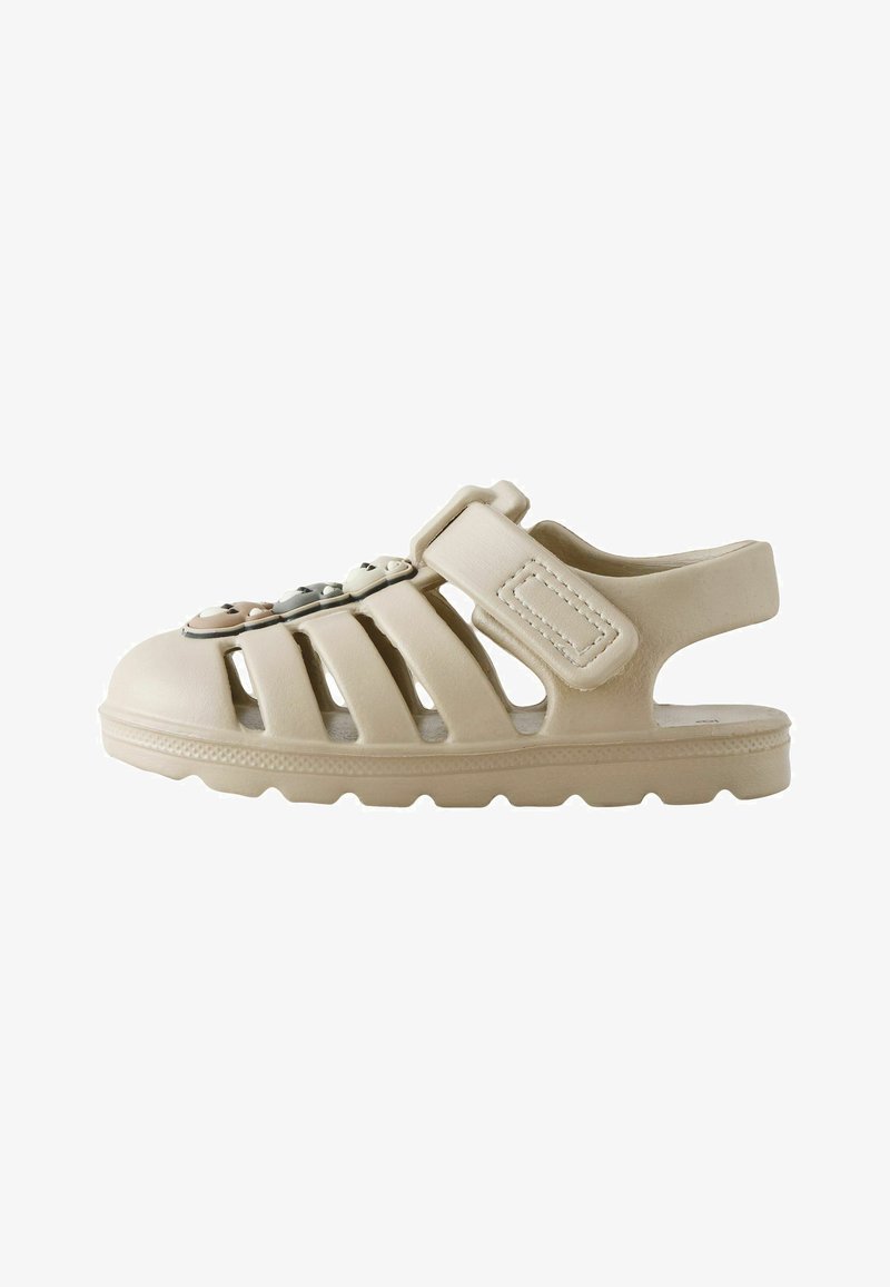 Sandalo beige chiuso con cinturino regolabile e ciondoli decorativi a forma di orsetto sulla parte superiore, progettato per un uso casual e una buona ventilazione.