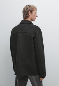 Zwarte wollen mix jas met een klassieke kraag en geruite manchetten, met een ontspannen pasvorm en een gladde textuur. Achteraanzicht toont een eenvoudig ontwerp.