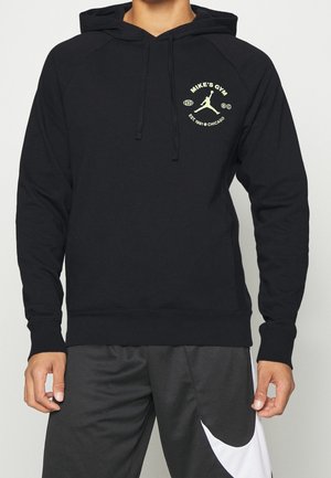 Černá mikina s kapucí s logem "Mike's Gym" a siluetou basketbalisty na levé straně hrudi, nošená s černo-bílými sportovními šortkami.