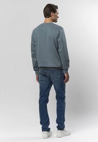 Szara bluza z okrągłym dekoltem i długimi rękawami, zestawiona z niebieskimi dżinsami i białymi trampkami. Gładka tekstura, swobodny design i luźny krój.