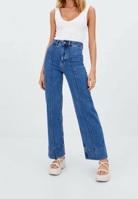 Hoge taille blauwe spijkerbroek met flared pijpen en contrasterende witte stiksels, voorzien van een knoopsluiting en brede pijpen.