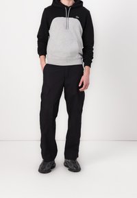 Felpa grigia e nera con tasca a marsupio, abbinata a pantaloni cargo neri con tasche laterali e scarpe da ginnastica nere con texture.