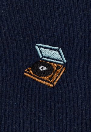 Motif brodé d'un tourne-disque vintage en marron et bleu clair sur tissu bleu foncé, avec un détail du disque et du couvercle ouvert.