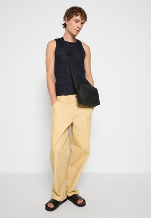 Top in maglia blu navy, pantaloni beige larghi, borsa a tracolla nera e sandali neri. Outfit casual con tessuti strutturati e colori neutri.