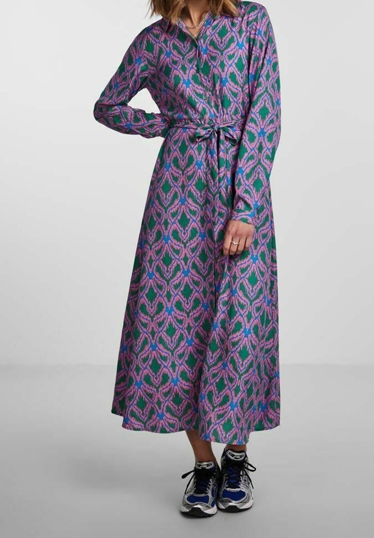 Lång knapp-up klänning med ett tyg i lila, rosa och gröna hjärtan, med knytmidja och långa ärmar, kombinerad med sportiga sneakers.