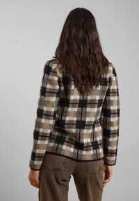 Giacca a quadri marrone e beige con maniche lunghe, tessuto testurizzato e silhouette aderente, abbinata a pantaloni marroni. Vista posteriore.