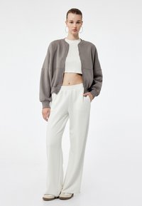 Overdimensioneret grå sweatshirt, hvid cropped top og cremede bukser med bred benvidde. Blødt, glat stof med elastisk talje og minimal detaljer.