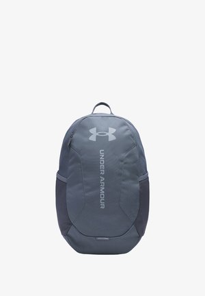 Pelēks mugursoma ar gludu tekstūru, ar Under Armour logotipu gaiši pelēkā krāsā, regulējamām siksnām un sānu kabatām uzglabāšanai.