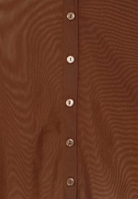 Brown fabric with a vertical row of five small, round, brownish-white buttons sewn in a straight line.