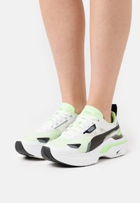 Baskets Puma en vert et blanc avec une tige en maille, un col rembourré et des accents noirs. Présente une semelle épaisse avec une texture anti-dérapante.