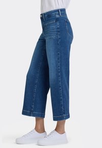 Högmidjade jeans med vida ben i mörkblå denim med en mjuk textur, avslutade fållar och bakfickor, kombinerade med vita sneakers.