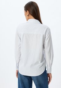 Camicia a maniche lunghe con bottoni, a righe blu chiaro e bianche, con orlo dritto e yoke posteriore. Materiale in cotone morbido con colletto classico.