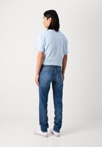 Lyseblå bomull t-skjorte, blå denimbukser og hvite sneakers. Buksene har en klassisk fem-lommers design.