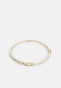 Brazalete de metal dorado con un acabado suave, que presenta una fila curva de cristales transparentes a lo largo de un lado. Logo grabado en el interior.