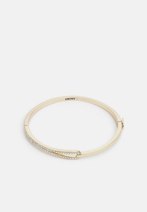 Brățară din metal auriu cu finisaj neted, având o linie curbată de cristale transparente pe o parte. Logo gravat în interior.