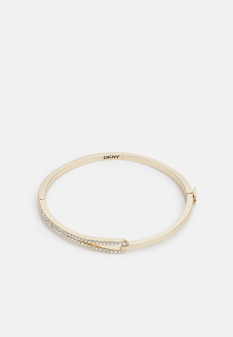Brazalete de metal dorado con un acabado suave, que presenta una fila curva de cristales transparentes a lo largo de un lado. Logo grabado en el interior.