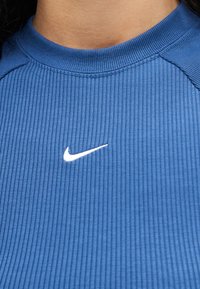 Κοντινό πλάνο ενός ατόμου που φοράει μπλε ριμπ μπλουζάκι με λευκό λογότυπο Nike Swoosh κεντραρισμένο κάτω από το λαιμό.