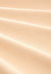 Ljus persikofärgad tyg med en texturerad yta, vikt för att visa en slät utseende som skapar subtila skuggor och ljusreflektioner.