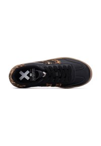 Zapatillas negras con un patrón de leopardo texturizado a lo largo de los lados, con un diseño de cordones negros y una suela de goma color caramelo.