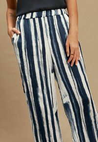 Striped pants in navy and white, featuring an elastic waistband, side pockets, and a textured fabric with vertical lines.