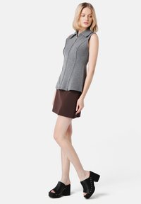 Gray sleeveless top with a front zipper, featuring a collared neckline and seam detailing, paired with a brown skirt and black platform shoes.