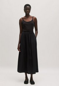 Zwart mouwloos topje gecombineerd met een vloeiende zwarte maxi rok, voorzien van een elastische tailleband en een gladde stofstructuur. Eenvoudige zwarte schoenen maken de look compleet.