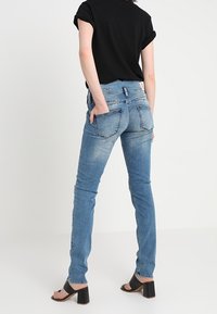 Modré džíny s úzkým střihem, vybledlým vzhledem, pěti kapsami a jemnými detaily v šití, spárované s černým tričkem a černými sandály na vysokém podpatku.