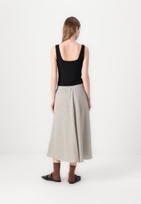 Svart ripstop tanktopp, stripete beigefarget og hvit midilengde skjørt, brune strømper og svarte leiligheter. Modell sett fra bak.
