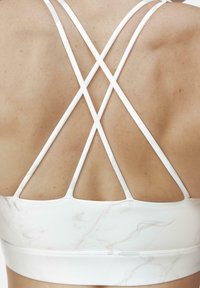 Top sportivo bianco con motivo marmorizzato, caratterizzato da spalline incrociate. Tessuto liscio e design aderente, che mette in mostra la schiena.