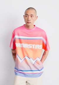 Short-sleeve, gradient t-shirt in pink and orange, featuring a bold white graphic "ANASTAS" and blue zigzag pattern across the bottom.