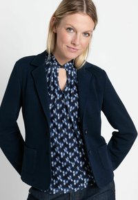 Navy blazer with two front pockets, textured fabric, and notched lapels, paired with a blue floral blouse featuring a keyhole front.