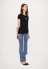 Tricou negru cu mânecă scurtă, cu logo pe piept, asortat cu blugi drepți de un albastru deschis și pantofi cu vârful ascuțit negri.