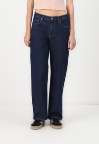 Jeans anchos de mezclilla oscura con diseño de cinco bolsillos, que presentan costuras contrastantes y un cierre de botón en la cintura.