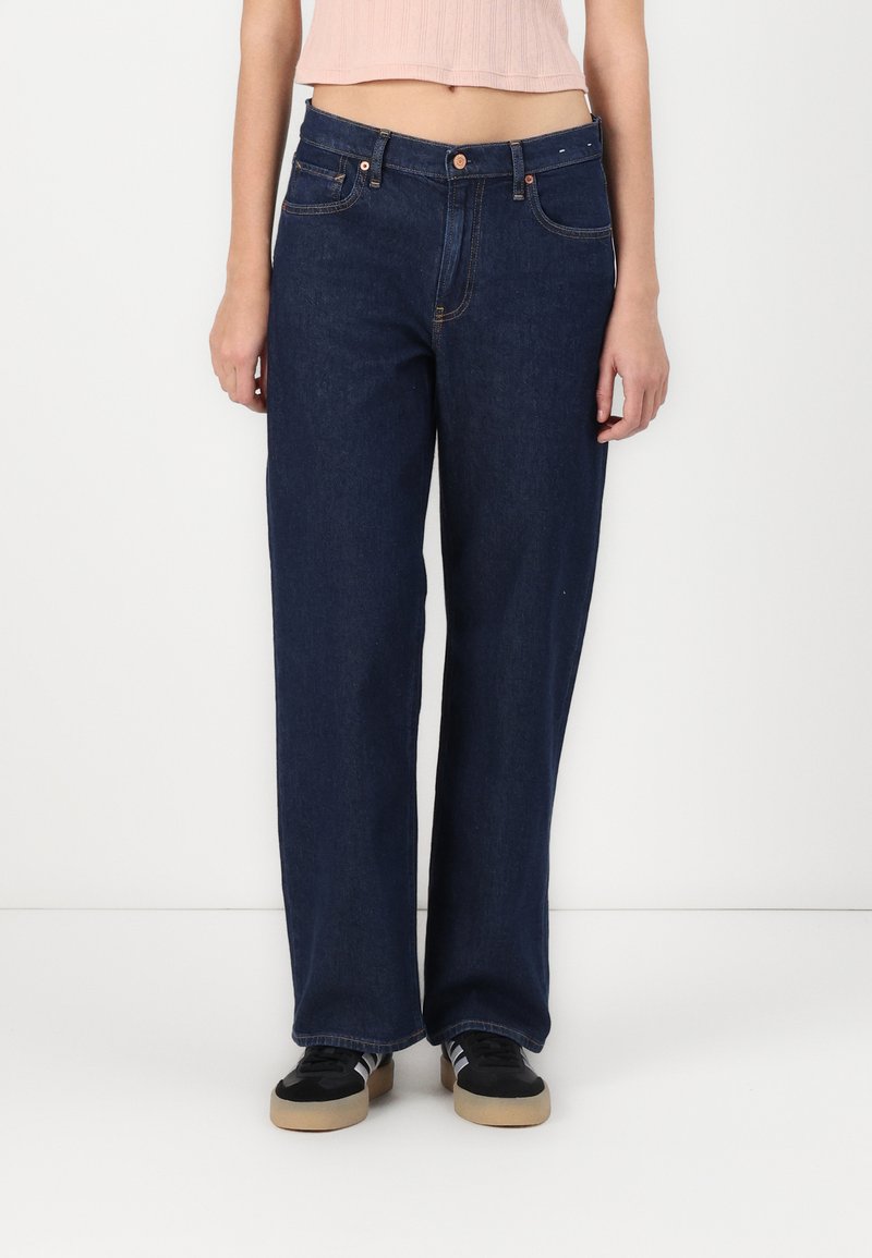 Jeans anchos de mezclilla oscura con diseño de cinco bolsillos, que presentan costuras contrastantes y un cierre de botón en la cintura.