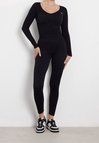 Schwarzes Langarmoberteil und Leggings aus einem strukturierten, glitzernden Material, kombiniert mit schwarz-weißen Sneakers mit kontrastierenden Akzenten.