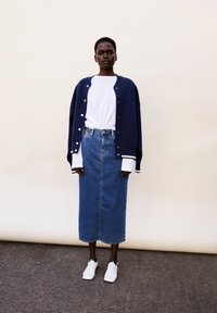 Cardigan de gran tamaño en color marino con botones blancos, llevado sobre una camiseta blanca, combinado con una falda de mezclilla larga y zapatillas blancas.