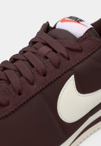Scarpa da ginnastica bordeaux con superiore testurizzato, logo Nike bianco e lacci abbinati. Presenta una linguetta imbottita e una suola di contrasto.