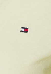 Helles, gelbes Baumwoll-T-Shirt mit einem kleinen, gestickten Logo in Marineblau, Weiß und Rot. Glatte Textur mit einer figurschmeichelnden Passform.