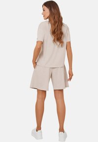 Beżowa bluzka z krótkim rękawem i dopasowane szorty z miękkiej, teksturalnej tkaniny, charakteryzujące się luźnym krojem, w połączeniu z białymi trampkami.