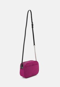 Borsa a tracolla imbottita magenta con tracolla nera regolabile, chiusura con zip e dettagli in catena argentata. Texture liscia e forma rettangolare.