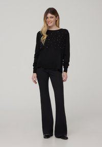 Pullover nero a maglia con decorazioni di perline, scollatura rotonda e maniche lunghe, abbinato a pantaloni neri a zampa d'elefante e scarpe nere.