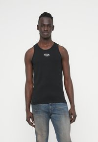 Μαύρο αμάνικο τοπ από βαμβάκι, με στρογγυλή λαιμόκοψη και μικρό λευκό λογότυπο στο στήθος. Συνδυάζεται με ξεθωριασμένο μπλε τζιν.