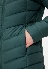 Zelená páperová bunda so prešívan�ými časťami, predným zipsom a bočnými vreckami, s hladkou, mäkkou textúrou.