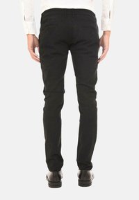 Pantaloni neri slim-fit con una texture liscia, due tasche posteriori e un elastico in vita. Indossati con scarpe nere e una camicia bianca a maniche lunghe.