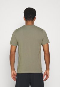 Camiseta de manga corta verde oliva con cuello redondo, textura suave y dobladillos cosidos. Detalles visibles de las costuras de los hombros y la espalda.