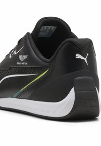 Czarne buty sportowe z perforowanym wzorem, białymi akcentami, zielono-niebieskim paskiem oraz logo Puma na pięcie. Teksturowana gumowa podeszwa.