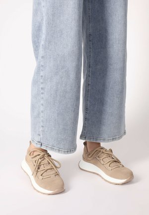 Beżowe sneakersy z teksturowanym zamszowym wierzchem, zawiązanym sznurowaniem i białą podeszwą środkową. Noszone z jasnoniebieskimi spodniami w szerokim kroju.