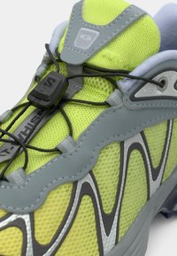 Limegrønn treningssko laget av mesh, med grå detaljer, et teksturert design og elastiske lisser med lås for sikker passform.